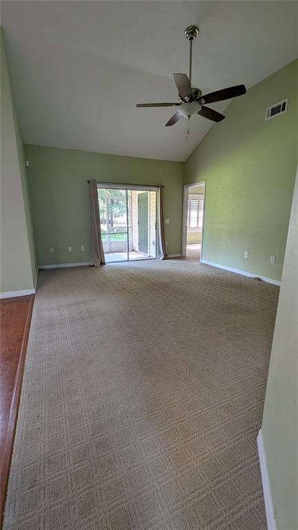 A living room with beige carpeting, vaulted ceilings, a ceiling fan, and sliding glass doors — 13200 W NEWBERRY ROAD UNIT Z144, NEWBERRY, FL