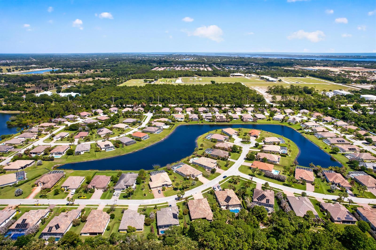 An aerial view shows a suburban neighborhood with houses surrounding a central lake — 7589 Fieldstone Ranch Square, Vero Beach FL 32967, VERO BEACH, FL