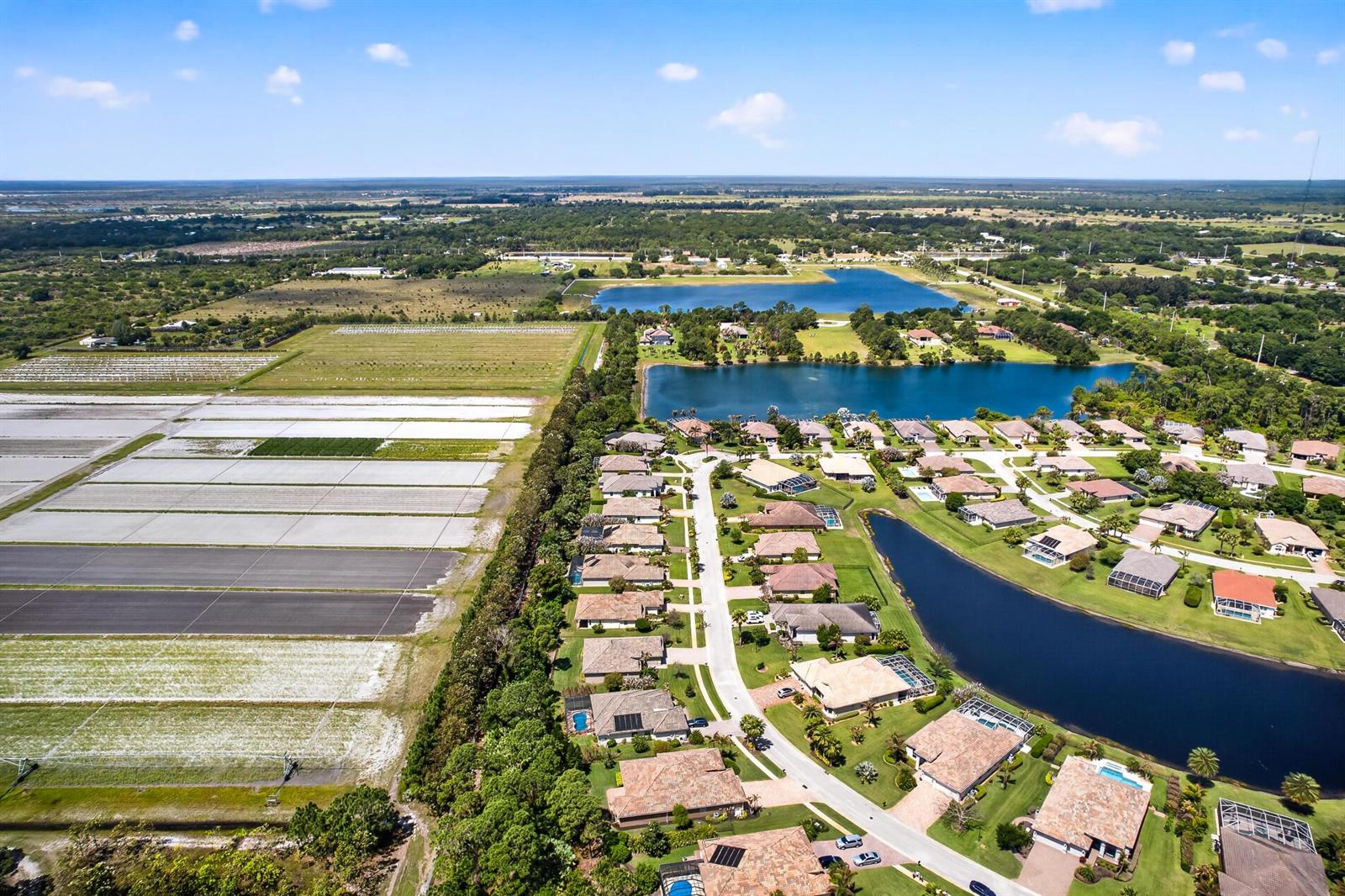 An aerial view shows a residential neighborhood bordering a large agricultural field and several lakes — 7589 Fieldstone Ranch Square, Vero Beach FL 32967, VERO BEACH, FL