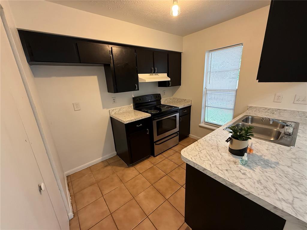 A kitchen features dark cabinets, a stainless steel stove, and white marble-patterned countertops — 2710 NE 23RD AVENUE, OCALA, FL