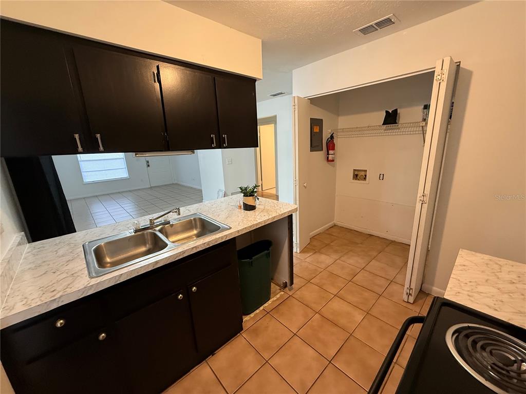A kitchen features dark cabinets, a marble-patterned countertop, a double sink, and an adjacent laundry closet — 2710 NE 23RD AVENUE, OCALA, FL