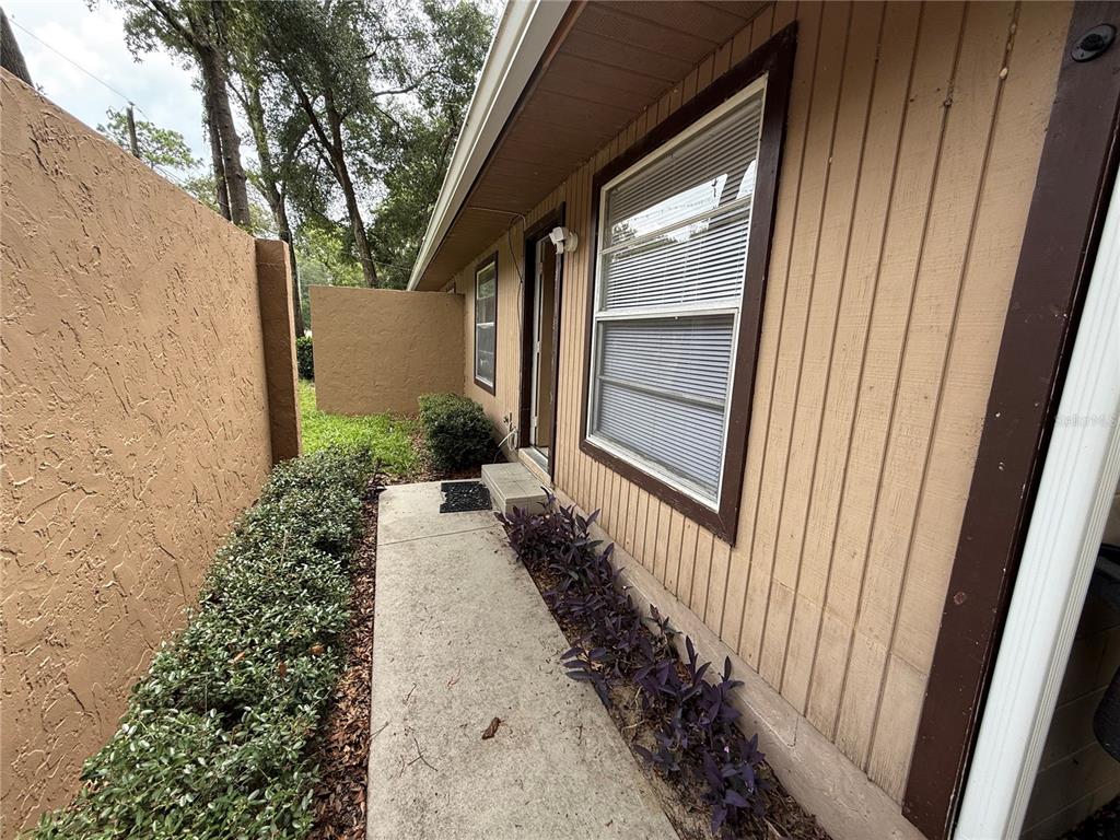 A concrete walkway leads to a doorway along the side of a tan wood-sided house — 2710 NE 23RD AVENUE, OCALA, FL