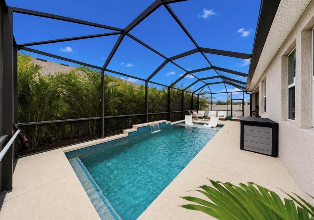 A screened-in patio features a rectangular swimming pool with a waterfall and lounge chairs — 11043 TAMARACK PLACE, PARRISH, FL