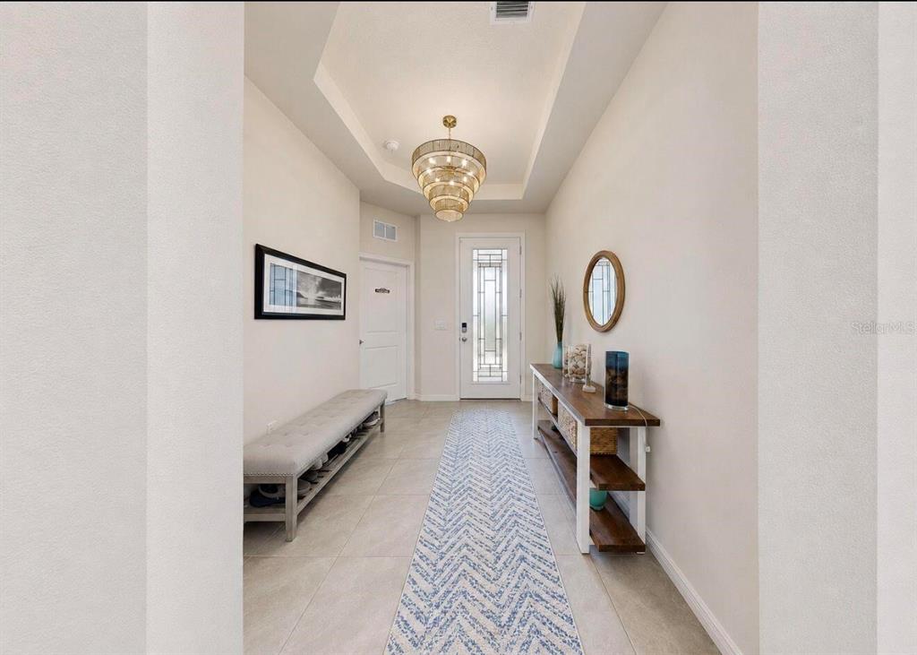 A bright entryway features a tray ceiling, a chandelier, a bench, and a console table — 11043 TAMARACK PLACE, PARRISH, FL