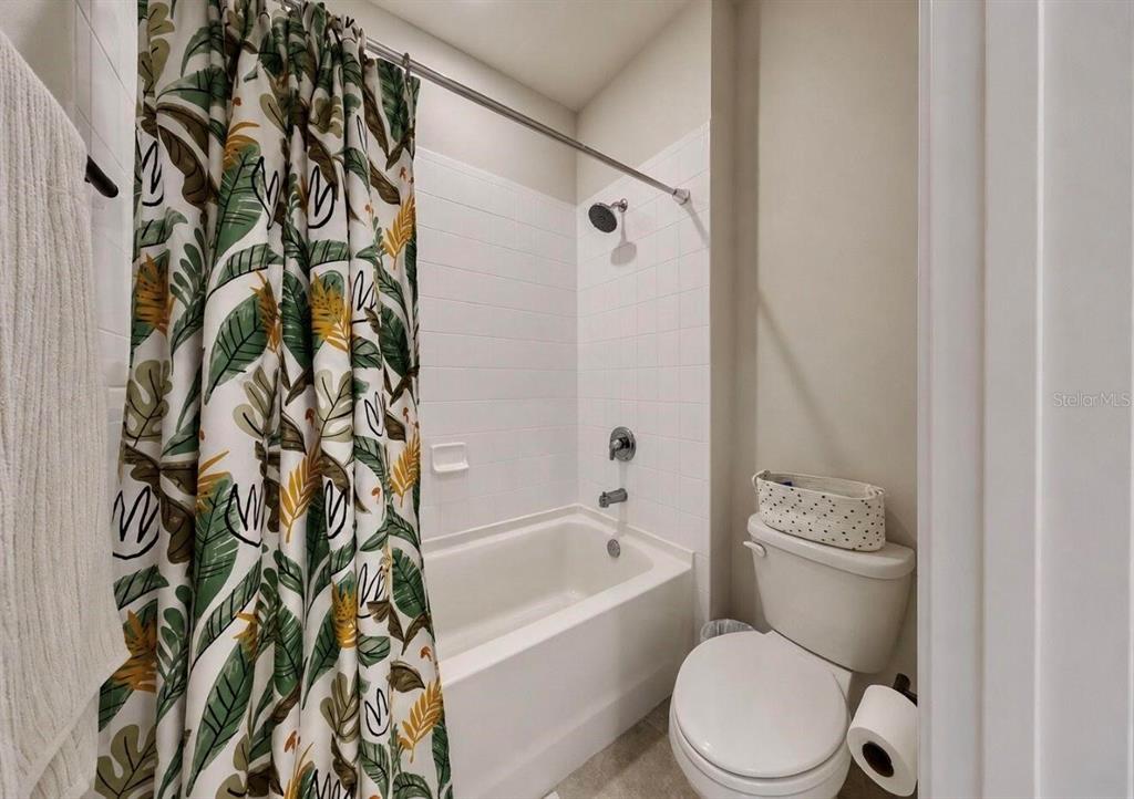 A bathroom features a white tiled shower-tub combination, a toilet, and a patterned shower curtain — 11043 TAMARACK PLACE, PARRISH, FL