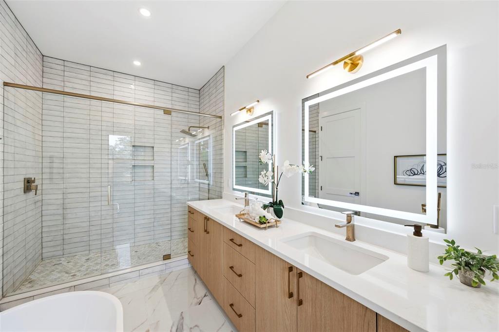 A modern bathroom features a glass-enclosed shower, double vanity with light wood cabinets, and mirrors — 6325 11TH AVENUE S, GULFPORT, FL