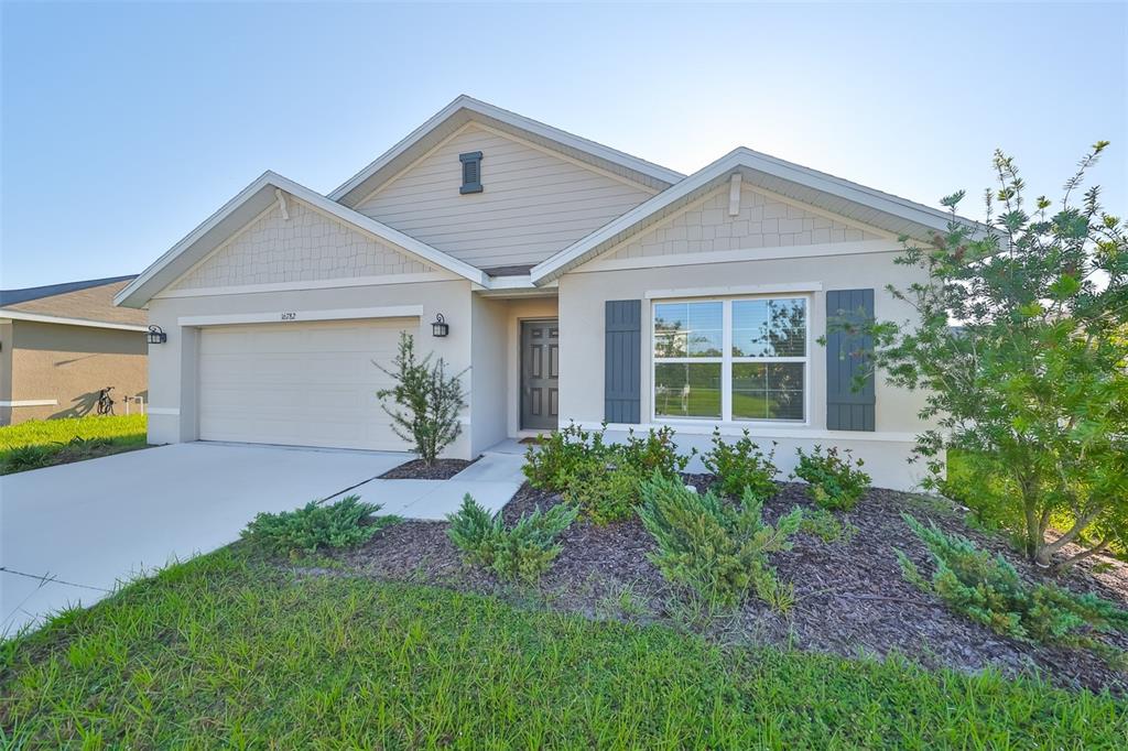 A single-story house with a beige stucco exterior, a two-car garage, and dark window shutters — 16782 CARLTON POND STREET, WIMAUMA, FL