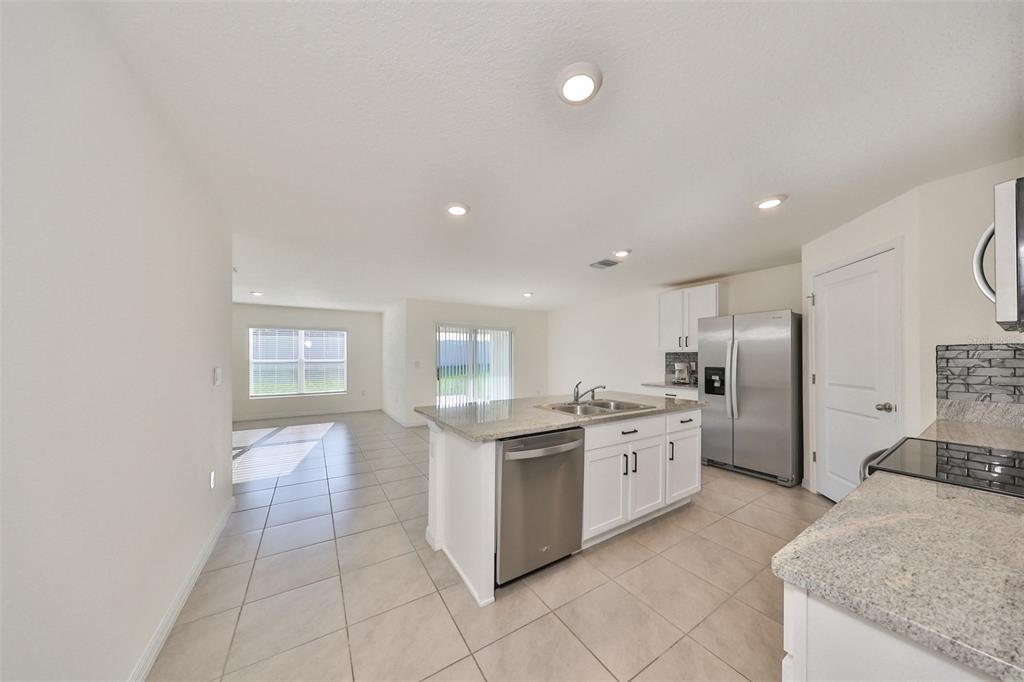 A kitchen with white cabinets, granite countertops, and stainless steel appliances opens to a living area — 16782 CARLTON POND STREET, WIMAUMA, FL