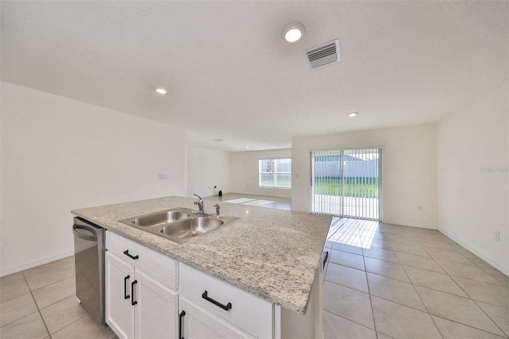 A kitchen island with a granite countertop and stainless steel sink overlooks an open living area — 16782 CARLTON POND STREET, WIMAUMA, FL