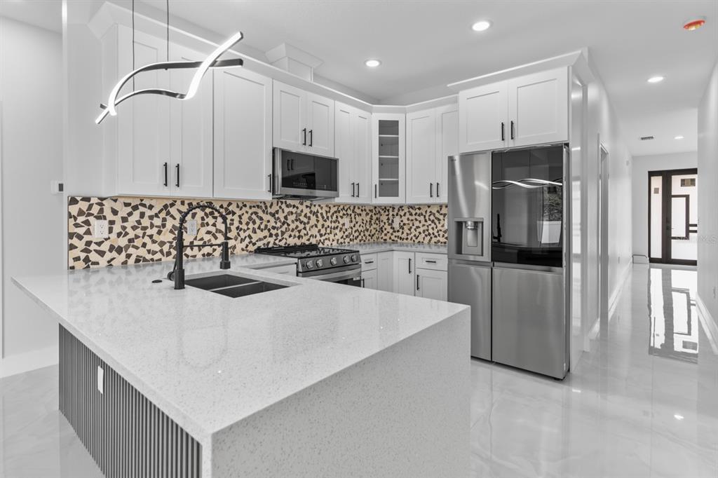 A modern kitchen features white cabinets, a quartz island, stainless steel appliances, and a mosaic backsplash — 8210 N ELMER STREET, TAMPA, FL