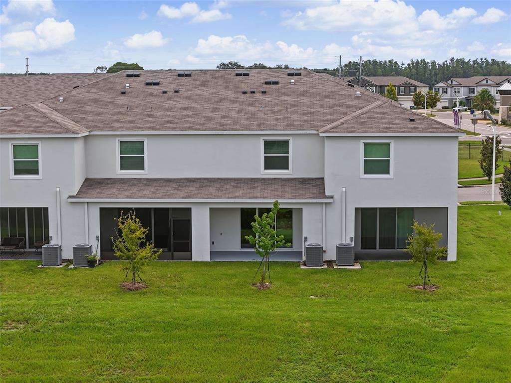 The rear exterior of a two-story townhouse features a grassy yard, screened patios, and AC units — 32612 TURTLE GRACE LOOP, WESLEY CHAPEL, FL