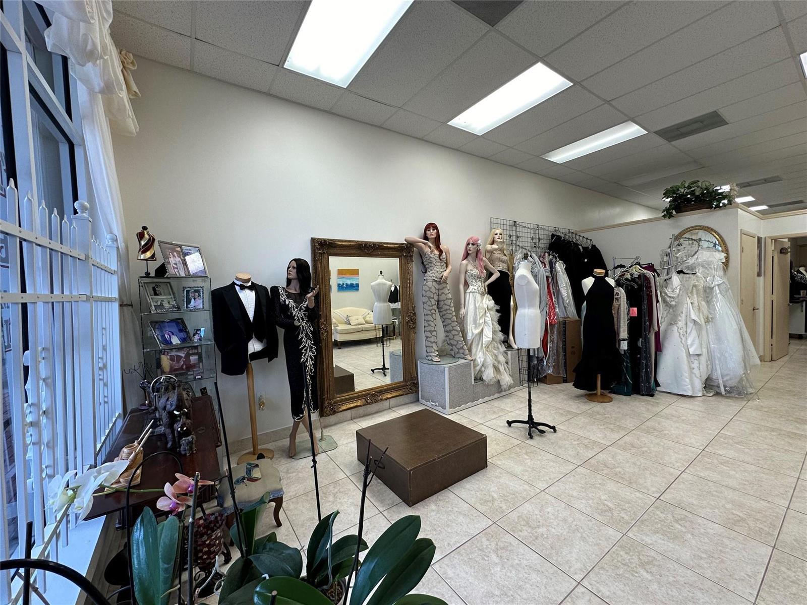 A retail space displays mannequins wearing formal attire, wedding dresses, and a large ornate mirror — CORAL SPRINGS, FL