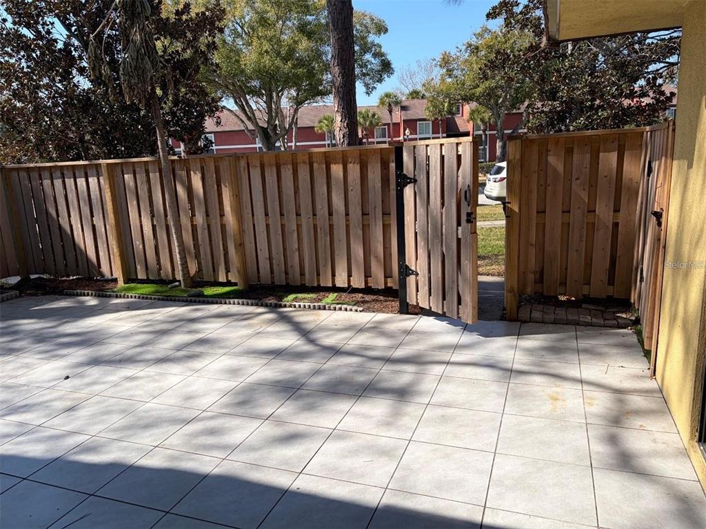 A paved patio features a wooden privacy fence with an open gate leading to a parking area — 5371 BAMBOO COURT UNIT 401, ORLANDO, FL