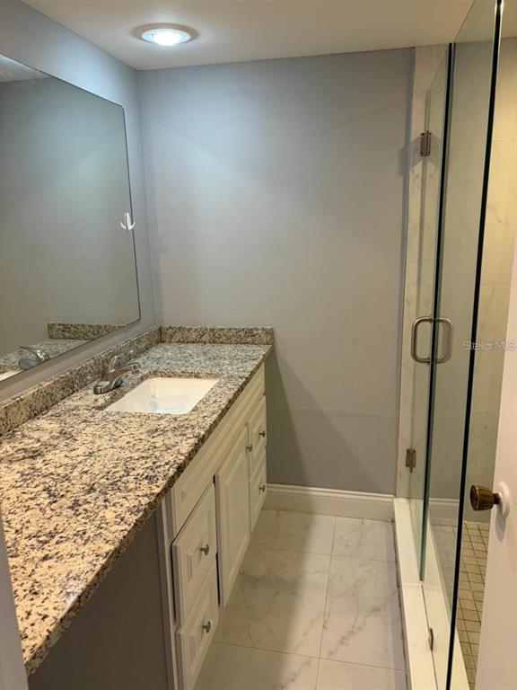 A bathroom features a granite vanity countertop, a white sink, and a glass-enclosed shower — 5371 BAMBOO COURT UNIT 401, ORLANDO, FL