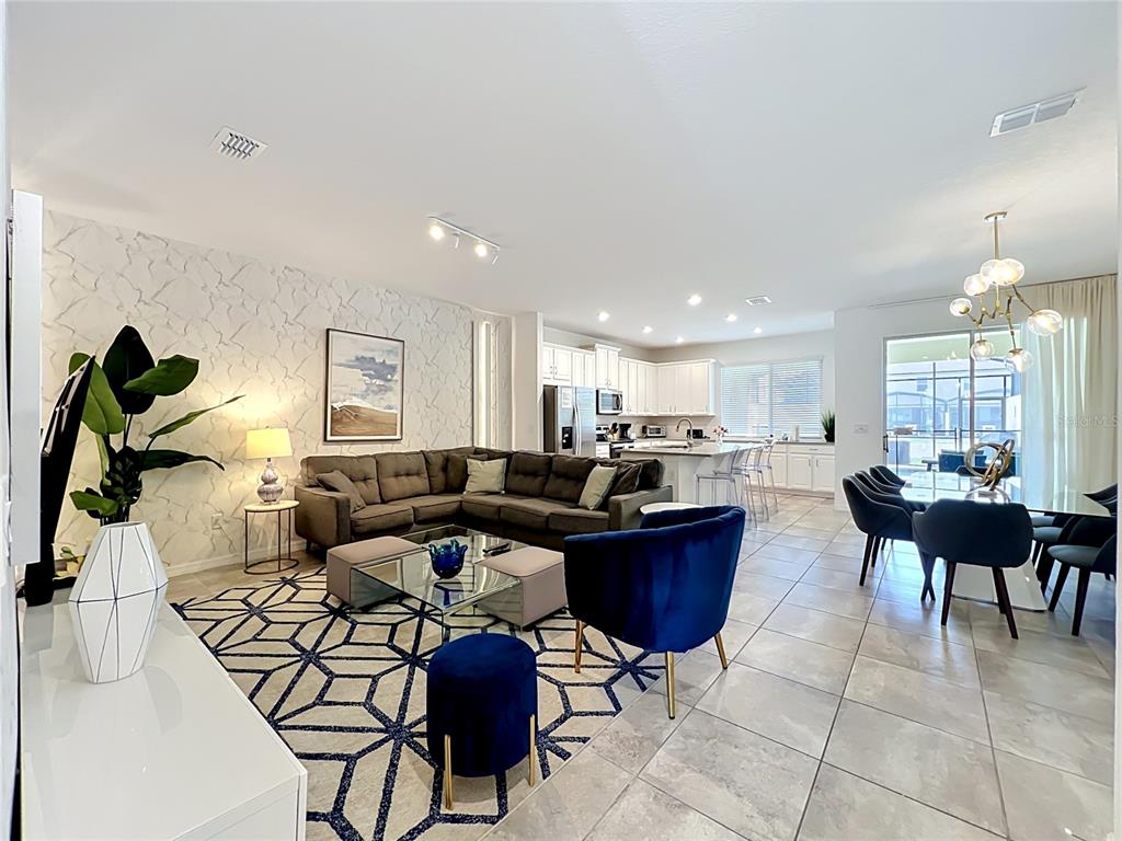 An open-concept living and dining area features a sectional sofa, tiled floors, and modern lighting — 8976 AMELIA DOWNS TRAIL, KISSIMMEE, FL