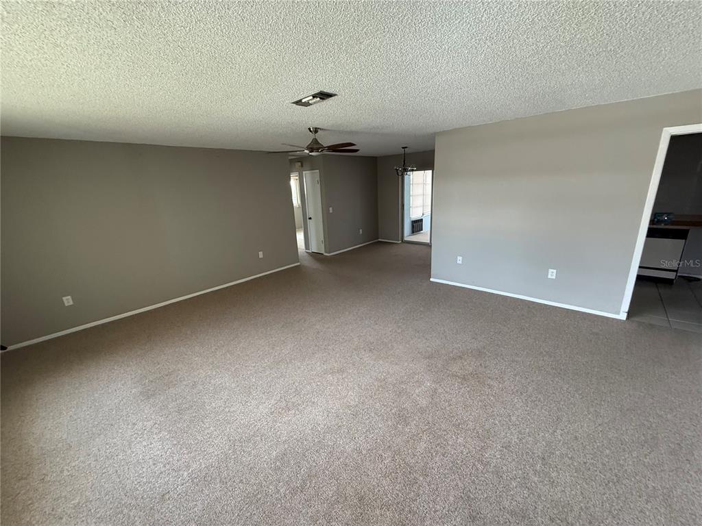 An empty living room features beige carpeting, gray walls, and a ceiling fan — 4212 NEIL LANE, BRADENTON, FL