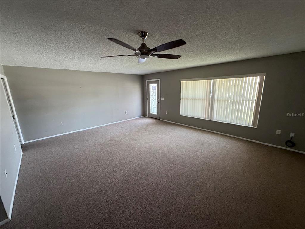 A spacious, carpeted living room features a ceiling fan, a glass-paneled door, and large windows — 4212 NEIL LANE, BRADENTON, FL