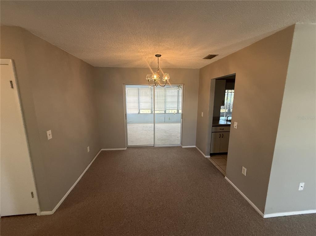 A dining area with beige carpet, a chandelier, and sliding glass doors leading to a lanai — 4212 NEIL LANE, BRADENTON, FL