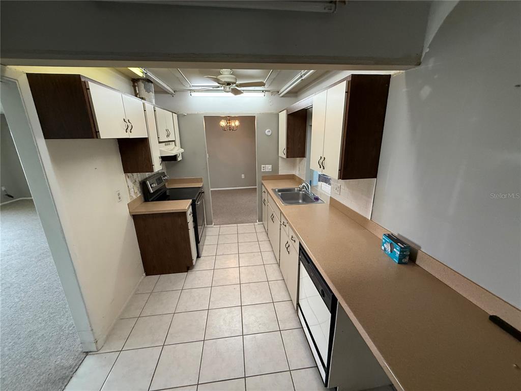 A galley kitchen features white cabinets, brown countertops, tiled flooring, and a stainless steel sink — 4212 NEIL LANE, BRADENTON, FL