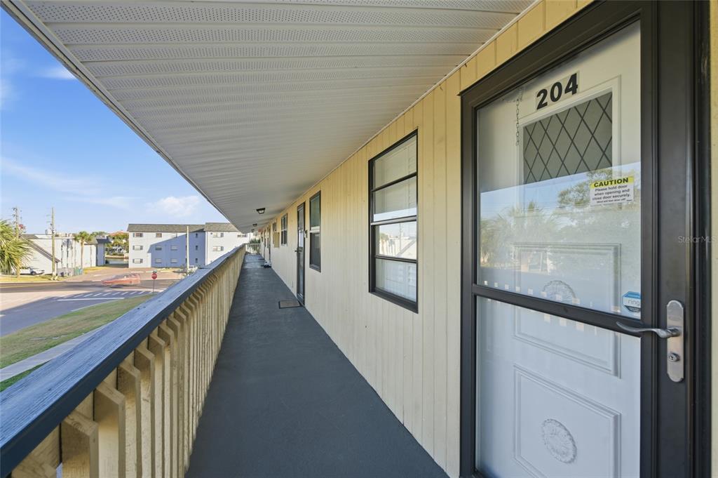 An exterior walkway with a wooden railing leads to the entrance of apartment unit 204 — 11650 CAPRI CIRCLE S UNIT 204, TREASURE ISLAND, FL