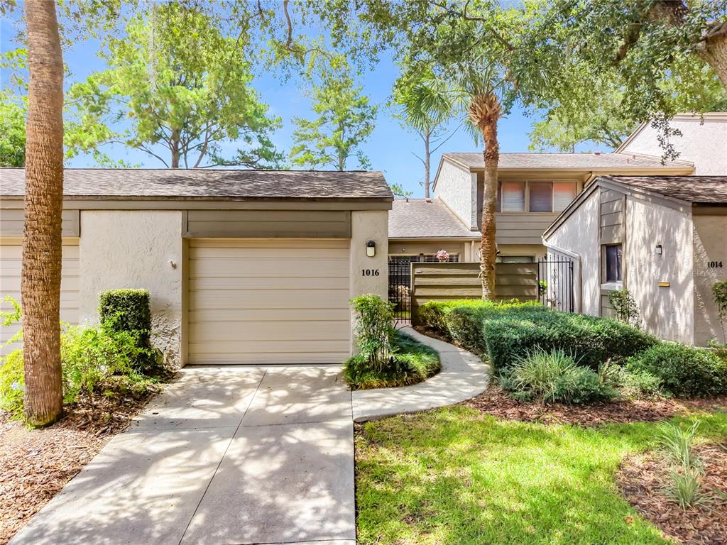 A beige garage with a concrete walkway leading to a gated entrance and landscaping — 1016 SHERRYWOOD STREET, CASSELBERRY, FL