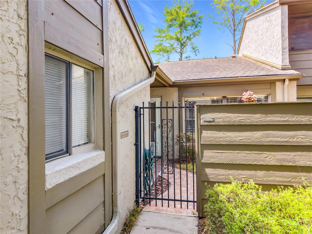 A metal gate leads to a paved walkway between two tan exterior walls — 1016 SHERRYWOOD STREET, CASSELBERRY, FL