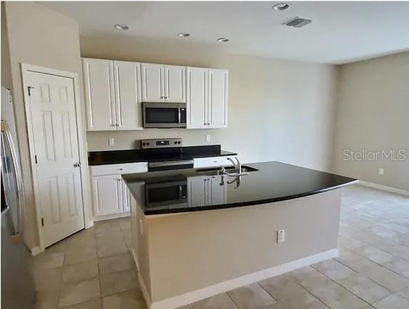A kitchen features white cabinets, black countertops, a center island with a sink, and tile flooring — 7027 TOWNE LAKE ROAD, RIVERVIEW, FL