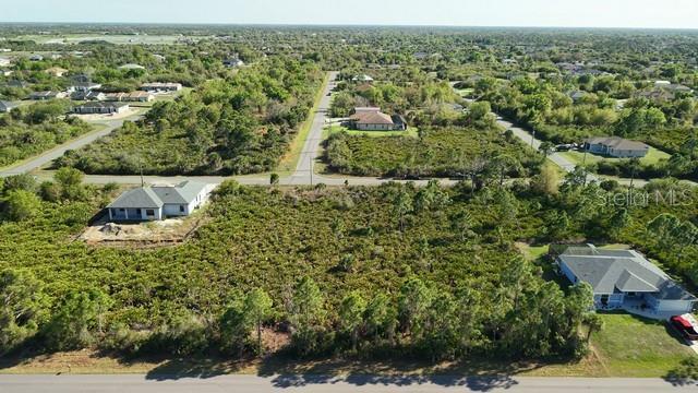An aerial view shows a vacant residential lot surrounded by trees and neighboring houses — 12154 ZITTLE AVENUE, PORT CHARLOTTE, FL