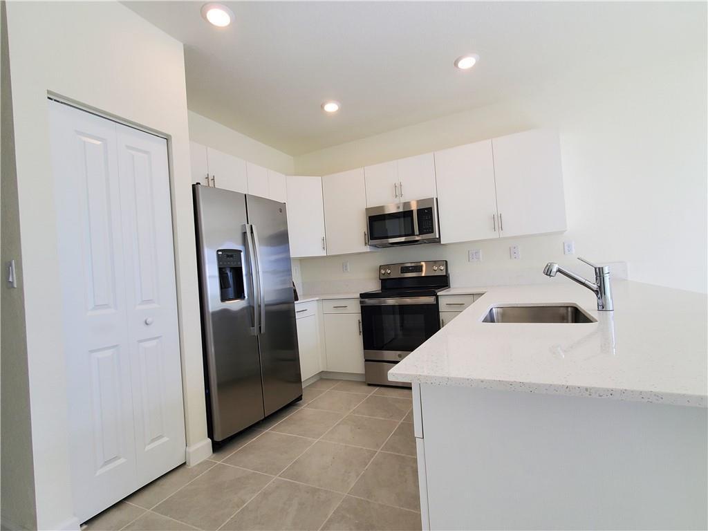 A kitchen features white cabinets, stainless steel appliances, and a quartz-topped island with a sink — 3216 W 114th Terrace, Hialeah FL 33018, HIALEAH, FL