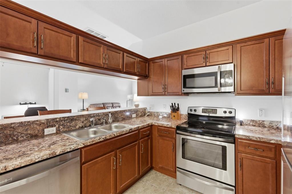 A kitchen features wood cabinets, granite countertops, and stainless steel appliances — 11214 PORT DOUGLAS DRIVE, NEW PORT RICHEY, FL