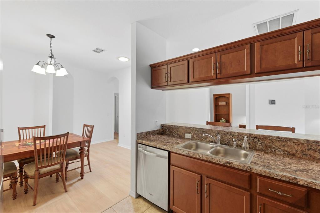 A kitchen with wood cabinets and granite countertops overlooks a dining area with wood flooring — 11214 PORT DOUGLAS DRIVE, NEW PORT RICHEY, FL