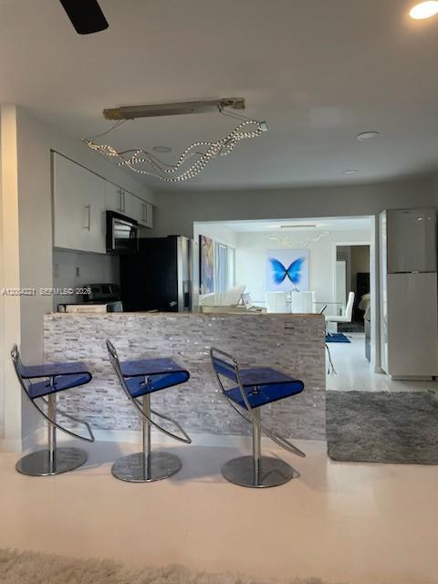 A kitchen features a stone-tiled breakfast bar with three blue acrylic stools and modern lighting — 3219 Buckley Ave, Lake Worth FL 33461, LAKE WORTH, FL