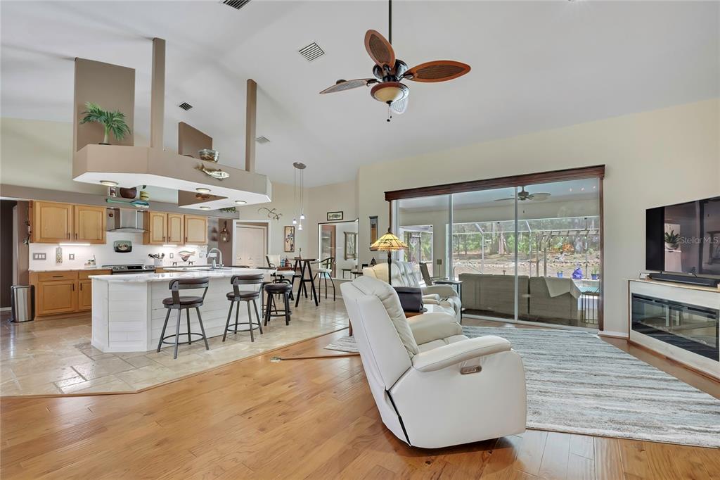 An open-concept kitchen and living area features light wood floors, white cabinetry, and sliding doors — 5701 W CHIVE LOOP, HOMOSASSA, FL