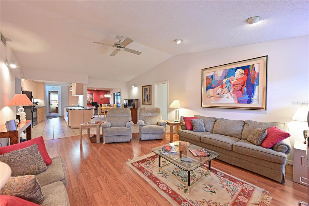 A living room with hardwood floors, a large area rug, and an open kitchen beyond — 4322 PASADENA COURT, SARASOTA, FL
