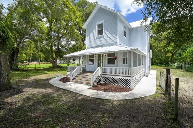 A two-story light blue house features a wraparound porch with white railings and lattice skirting — 37315 TRILBY ROAD, DADE CITY, FL
