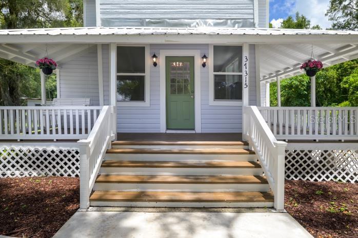 A light blue house features a green front door, wooden steps, and a wraparound porch — 37315 TRILBY ROAD, DADE CITY, FL