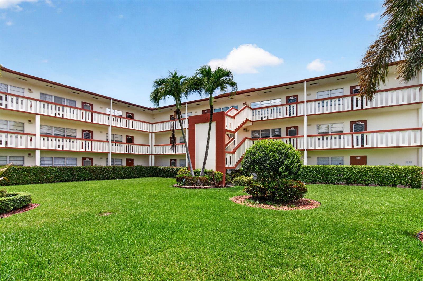 A three-story apartment building with exterior walkways and palm trees overlooks a grassy lawn — 374 Brighton I # 374, Boca Raton FL 33434, BOCA RATON, FL