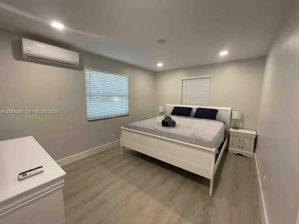 A bedroom features a white bed frame, light wood-look flooring, and a wall-mounted air conditioner — 1925 Dewey St # 1927, Hollywood FL 33020, HOLLYWOOD, FL