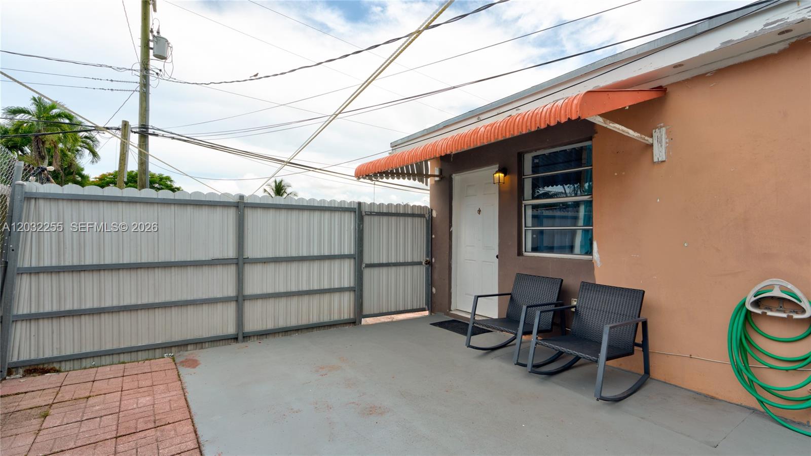 A patio area features two rocking chairs, a green garden hose, and a metal fence — 9840 SW 48th St, Miami FL 33165, MIAMI, FL