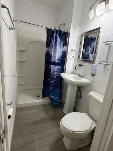 A bathroom features a walk-in shower with a patterned curtain, pedestal sink, and toilet — HIALEAH, FL