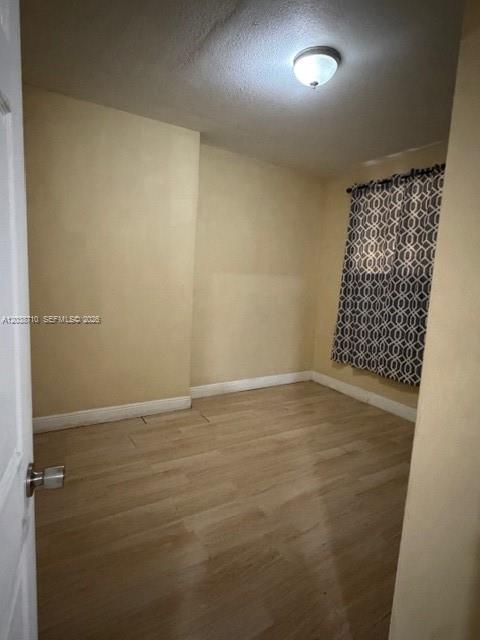 A small bedroom with light-colored walls, wood-look flooring, and a window with patterned curtains — HIALEAH, FL