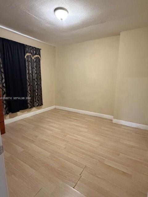 An empty bedroom features light wood-look flooring, beige walls, and dark patterned curtains — HIALEAH, FL