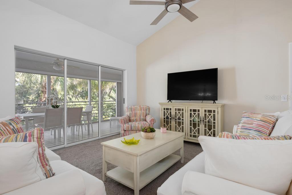 A living room features a vaulted ceiling, a television on a cabinet, and sliding doors — 6101 W 34TH STREET W UNIT 6D, BRADENTON, FL