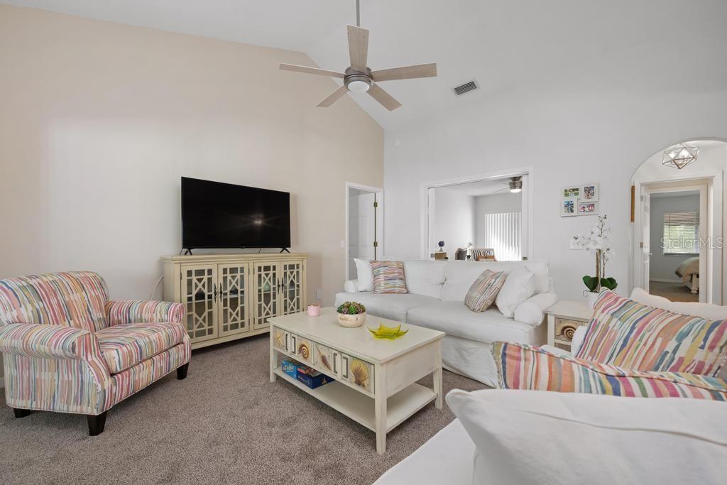 A living room features a vaulted ceiling, a ceiling fan, a white sofa, and patterned armchairs — 6101 W 34TH STREET W UNIT 6D, BRADENTON, FL