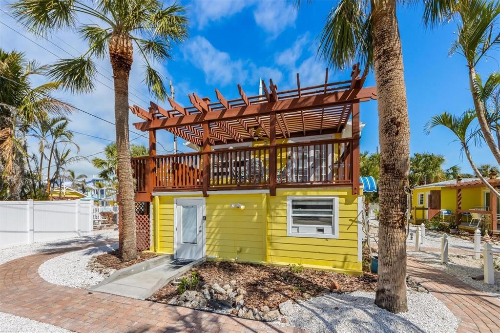 A yellow two-story house with a wooden deck and pergola stands among palm trees — 110 OAK AVENUE UNIT A, ANNA MARIA, FL