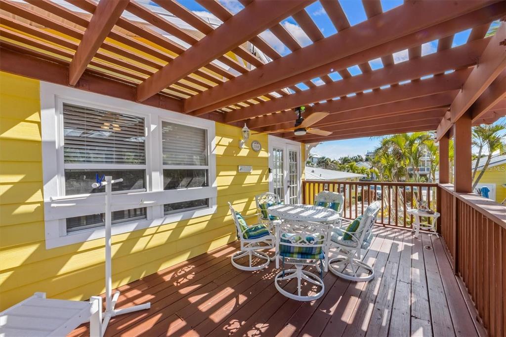 A wooden deck features a pergola, patio furniture, and yellow siding on a sunny day — 110 OAK AVENUE UNIT A, ANNA MARIA, FL