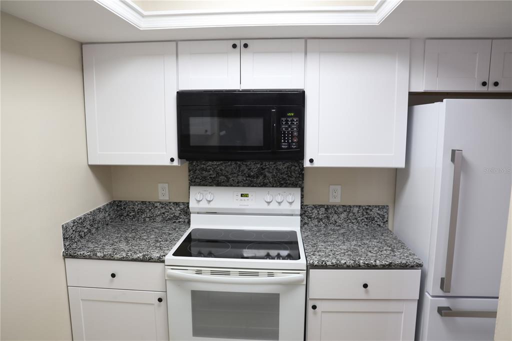 A kitchen features white cabinets, granite countertops, a black microwave, and a white electric stove — 5831 SW 9TH PLACE, GAINESVILLE, FL