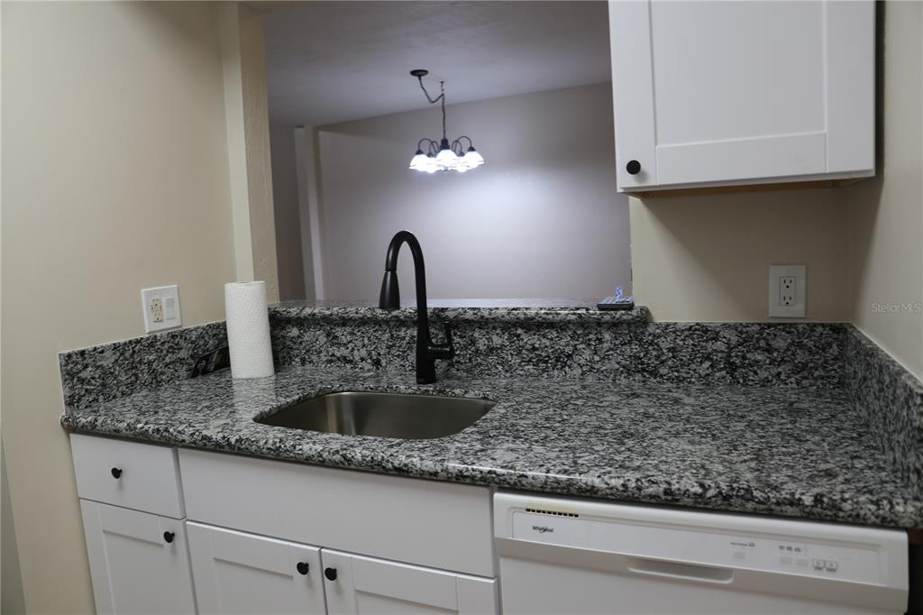 A kitchen sink with a black faucet and granite countertops sits below a pass-through window — 5831 SW 9TH PLACE, GAINESVILLE, FL