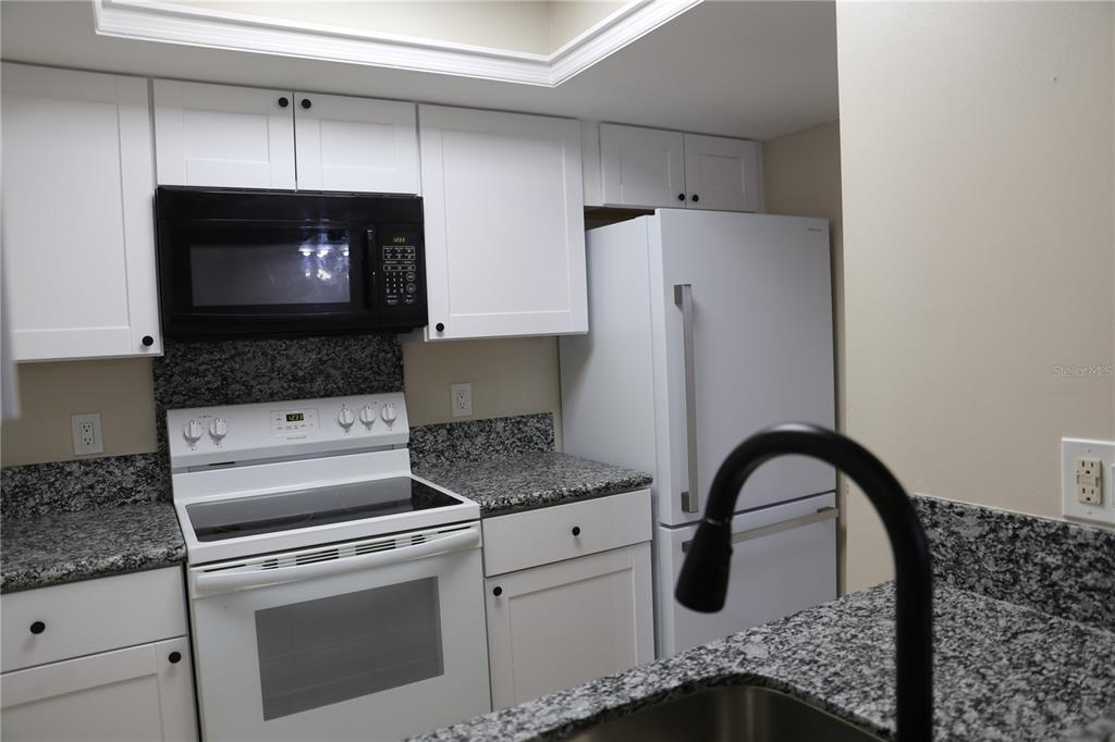A kitchen features white cabinets, granite countertops, a black microwave, and a white stove — 5831 SW 9TH PLACE, GAINESVILLE, FL