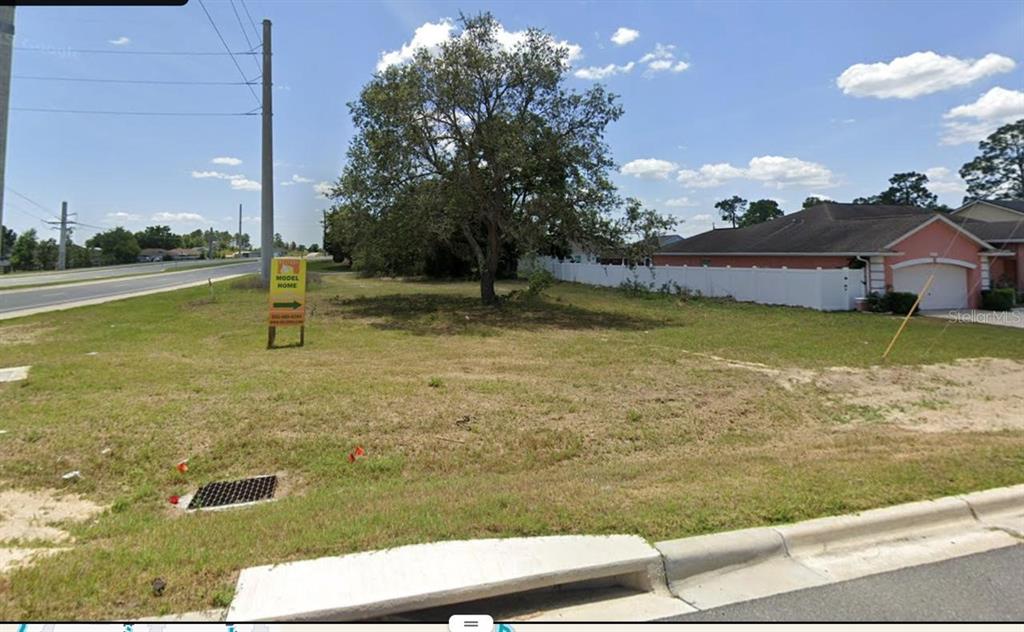 A vacant, grassy lot features a large tree and a model home sign near a road — LOT 9 SW 129TH PLACE, OCALA, FL